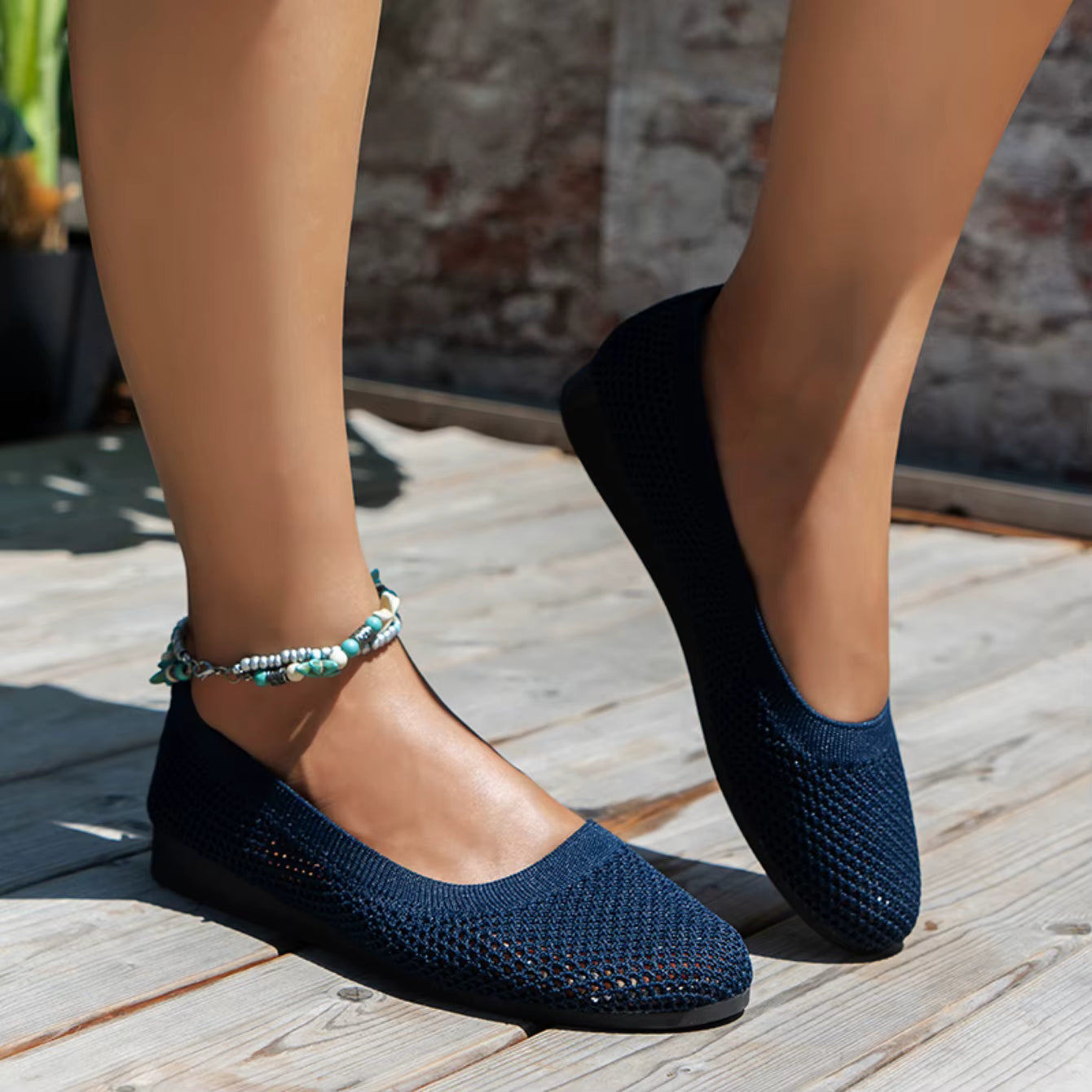 Navy blue flats worn on a wooden floor with a stone wall background