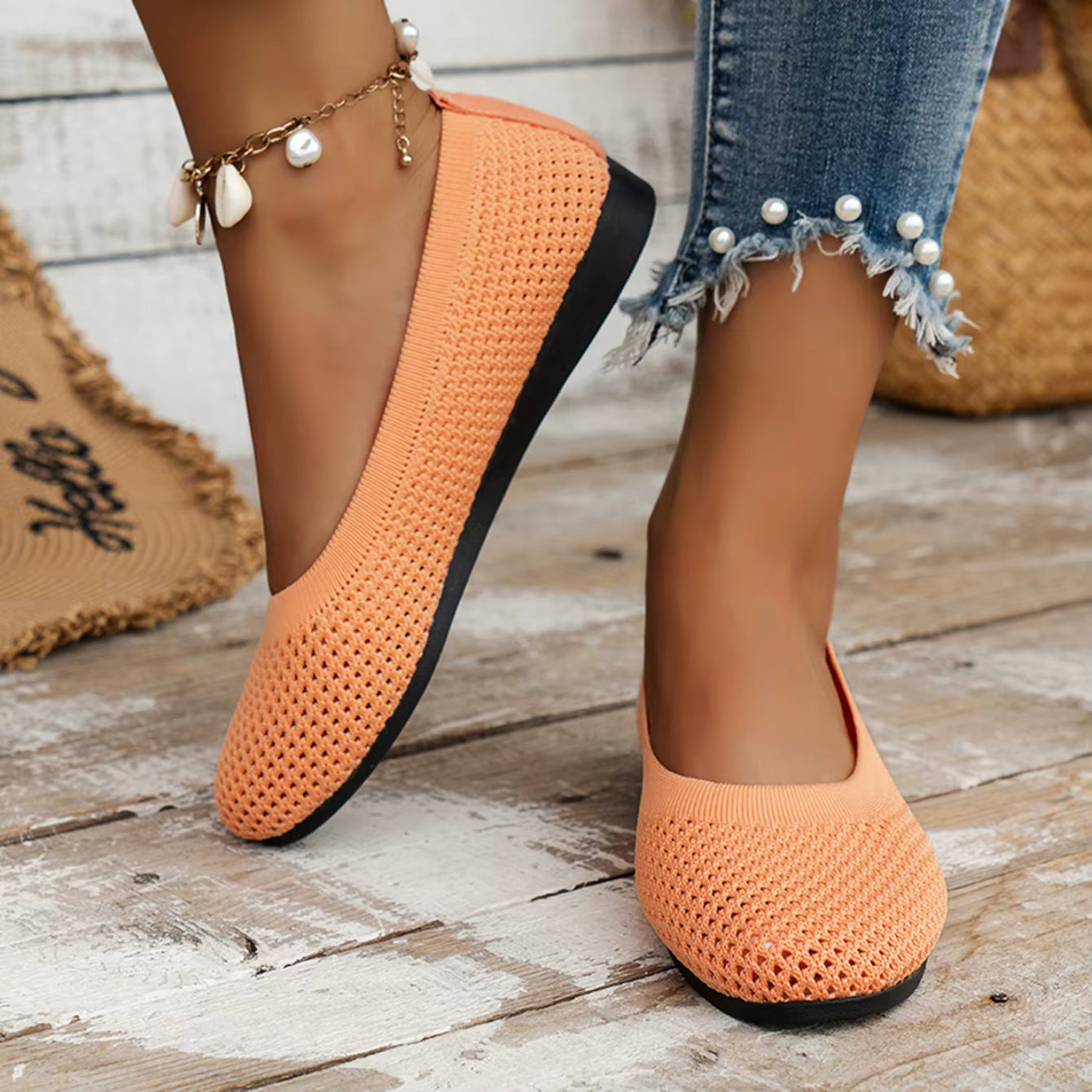 Orange woven shoes with black soles worn by a person on a wooden floor.