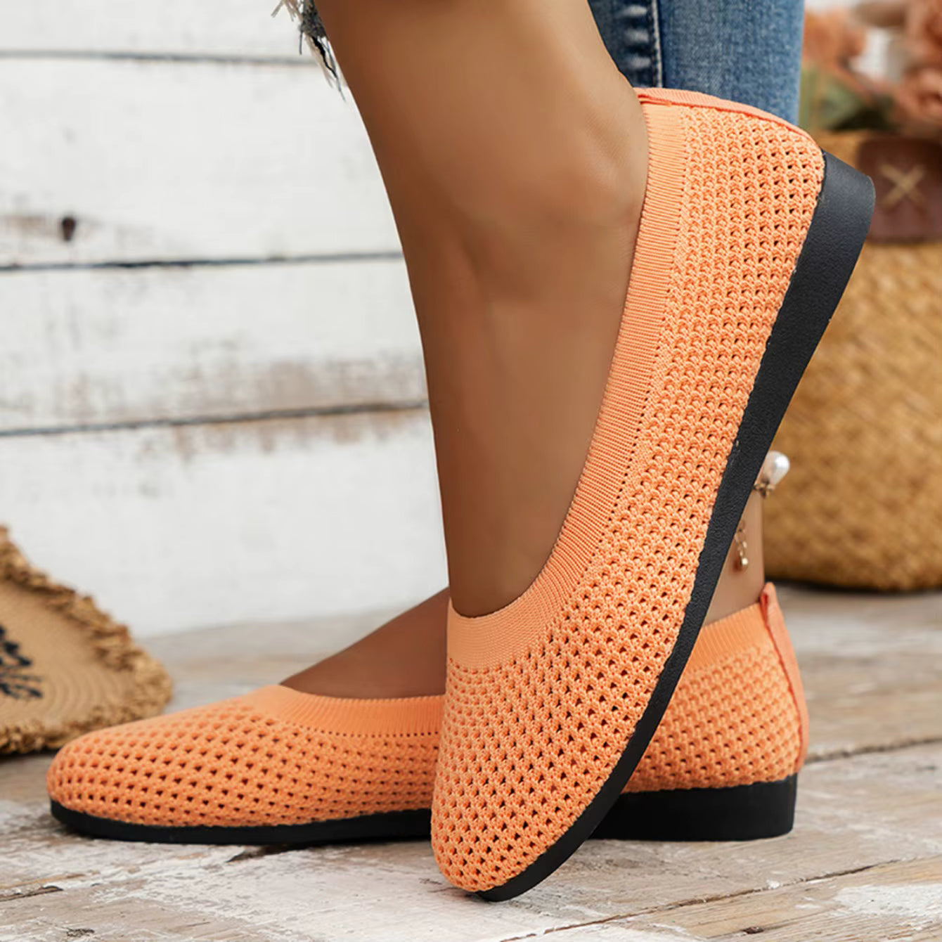 Orange woven shoes with black soles on a wooden floor.