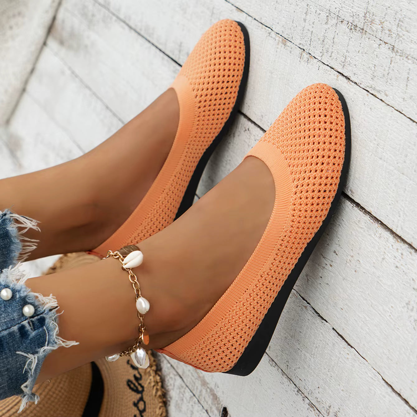 Orange flats worn on a light wooden floor with denim shorts and pearl bracelet.