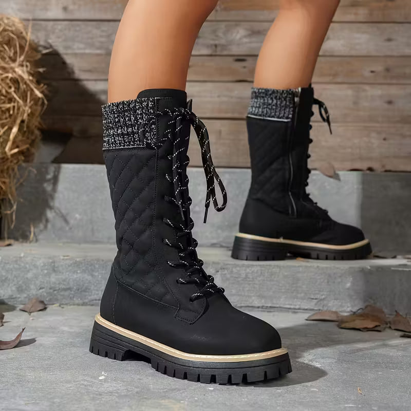 Black quilted knee-high boots with lace-up design worn by a person on steps.