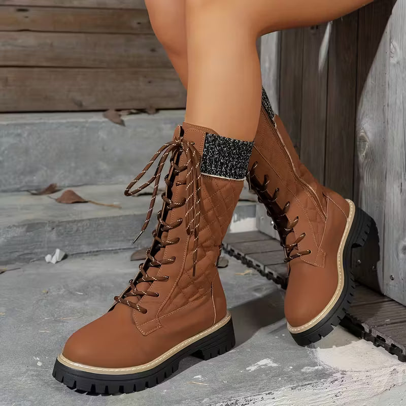 Brown lace-up boots worn by a person on a stone surface with wooden steps in the background.
