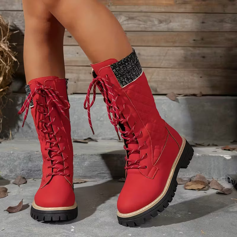 Red lace-up boots with black soles on a stone surface.