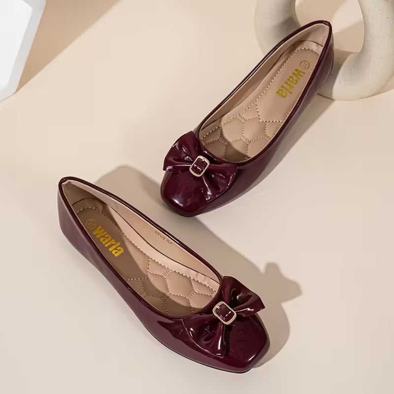 Pair of maroon shoes with bow details on a beige surface