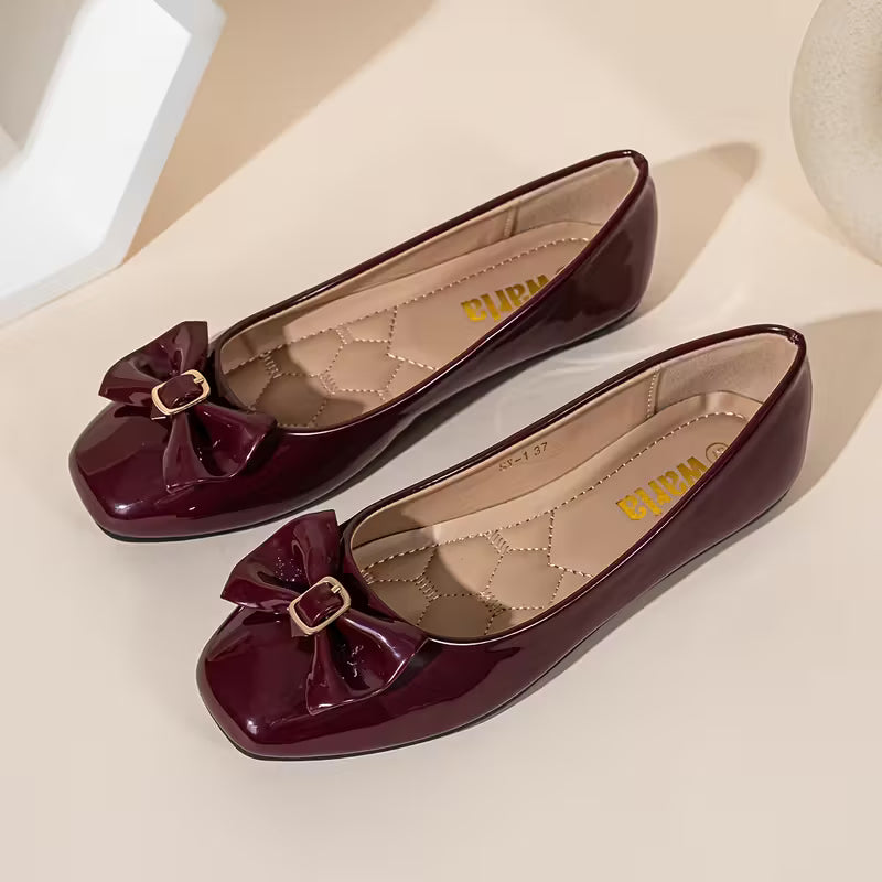 Pair of maroon flat shoes with bow details on a light beige background