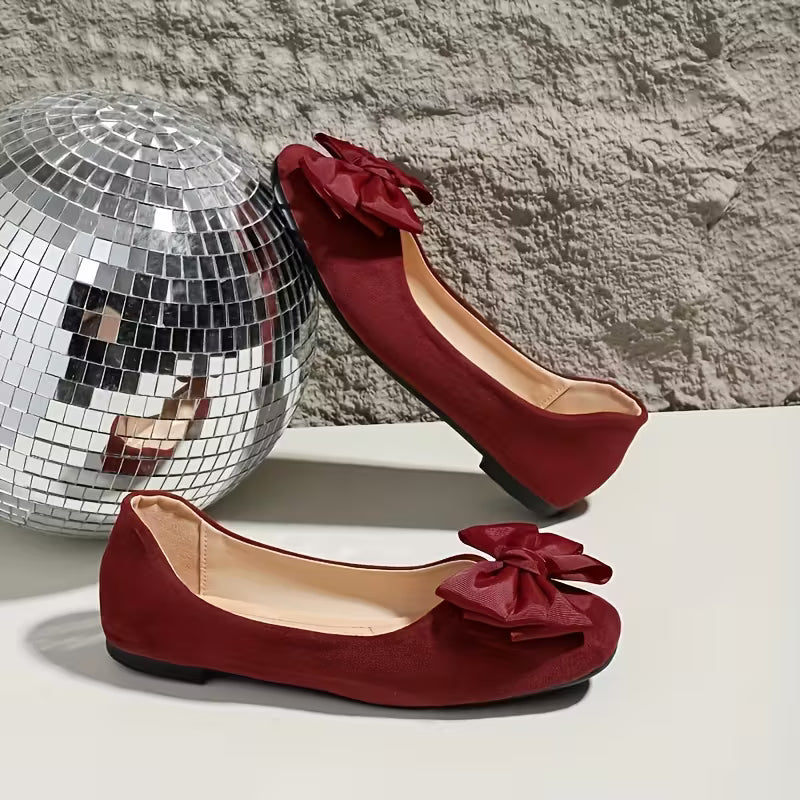 Red shoes with bow details next to a disco ball on a textured surface.