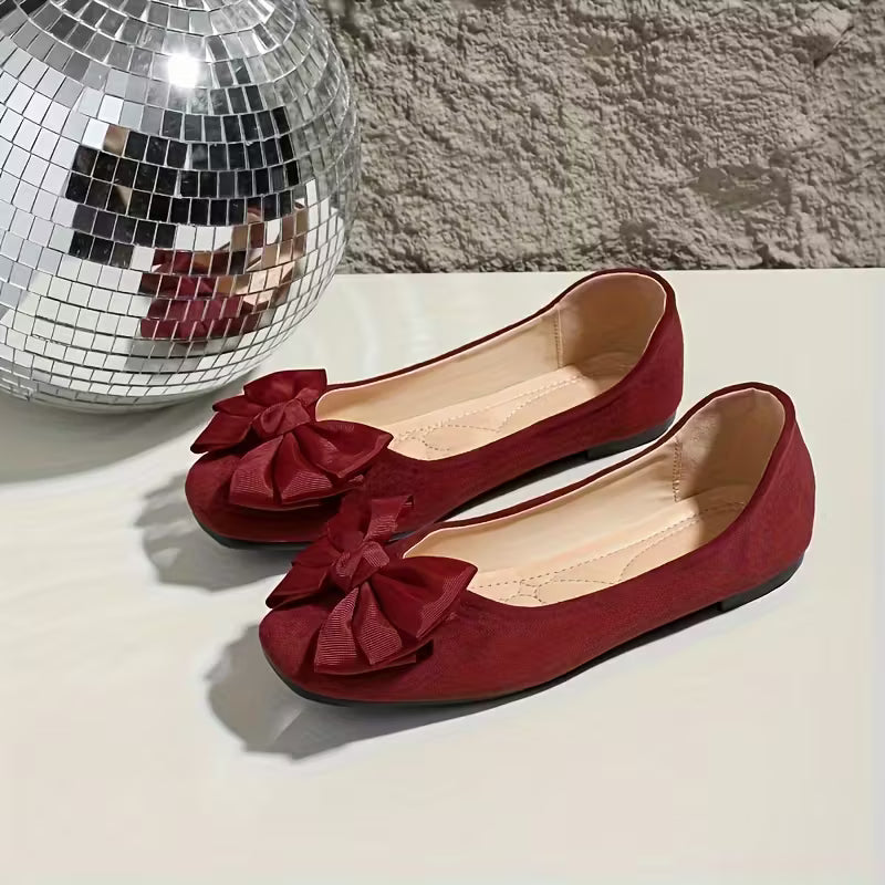 Red shoes with bow details on a light surface next to a disco ball.