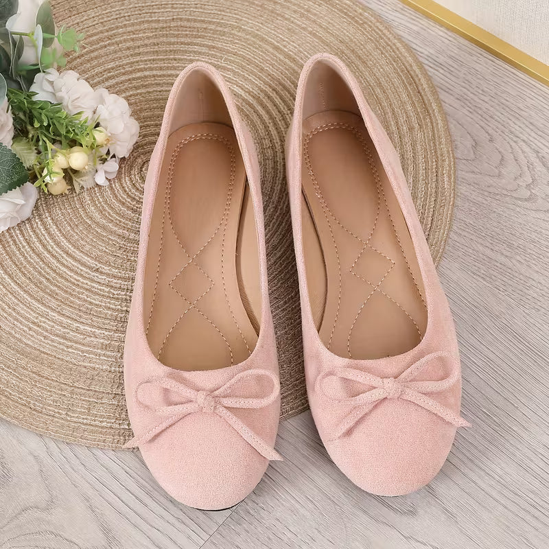 Pair of pink flats with bow details on a wooden surface.