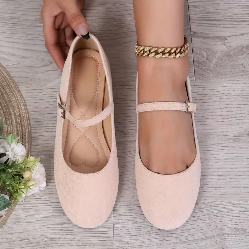 Pair of light pink flats on a wooden surface with a hand holding one shoe.