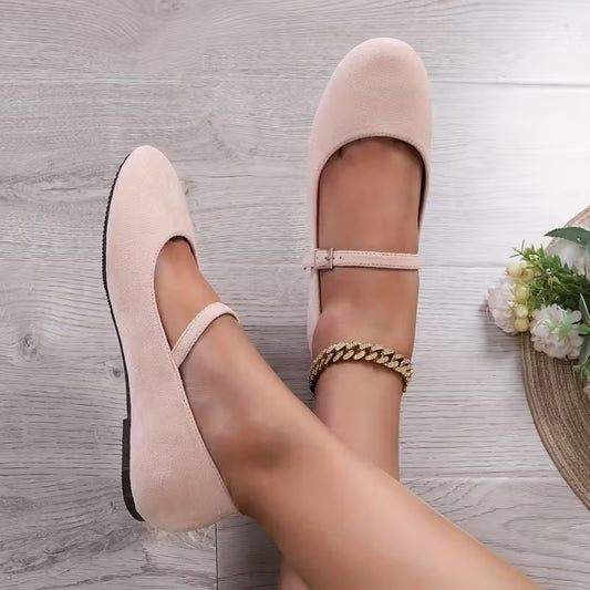 Beige flat shoes worn with a gold anklet on a wooden floor.