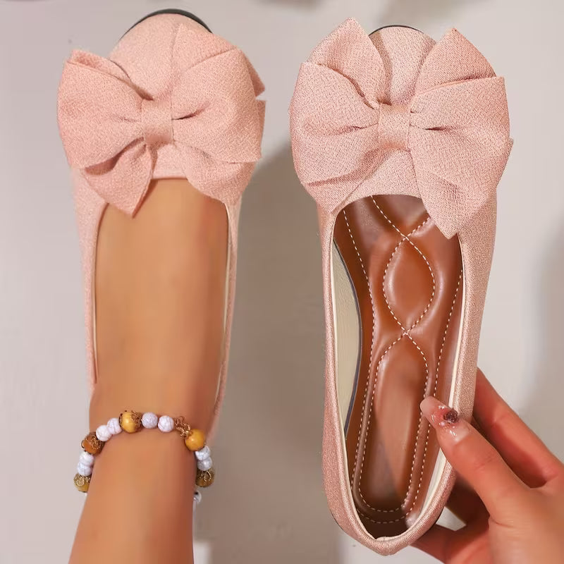Pink flats with large bows held by a hand against a neutral background