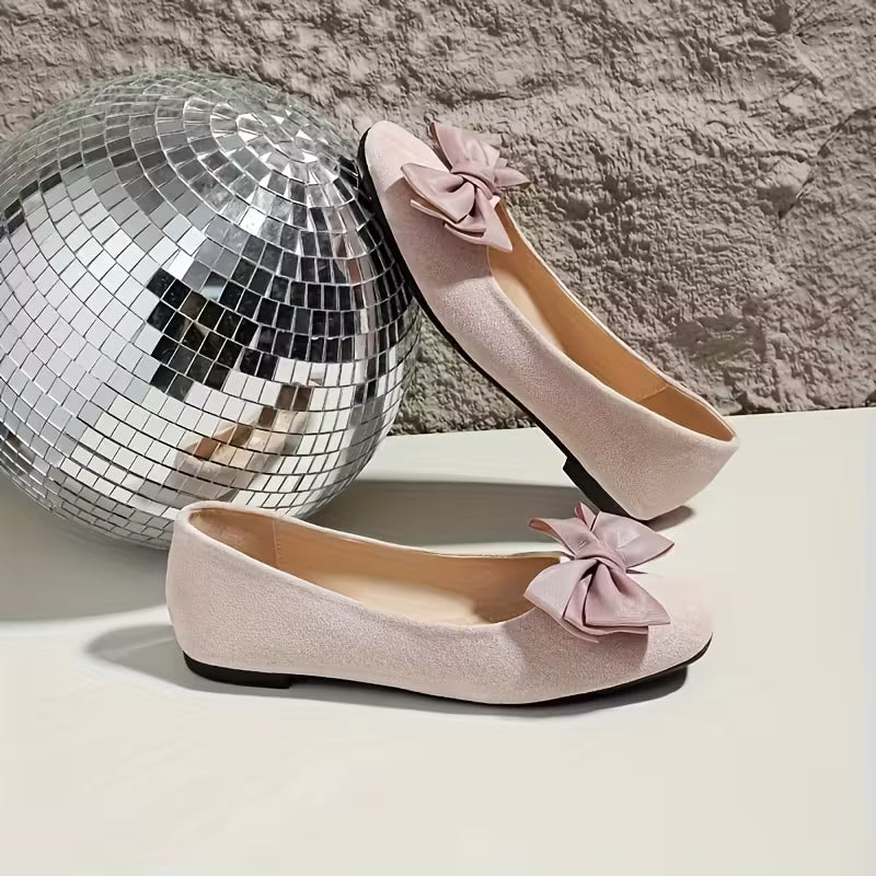 Pink shoes with bow details next to a disco ball on a textured surface