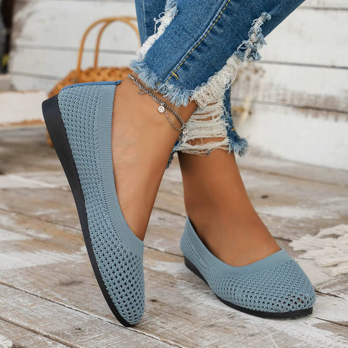 Blue woven flats worn with ripped jeans on a wooden floor.