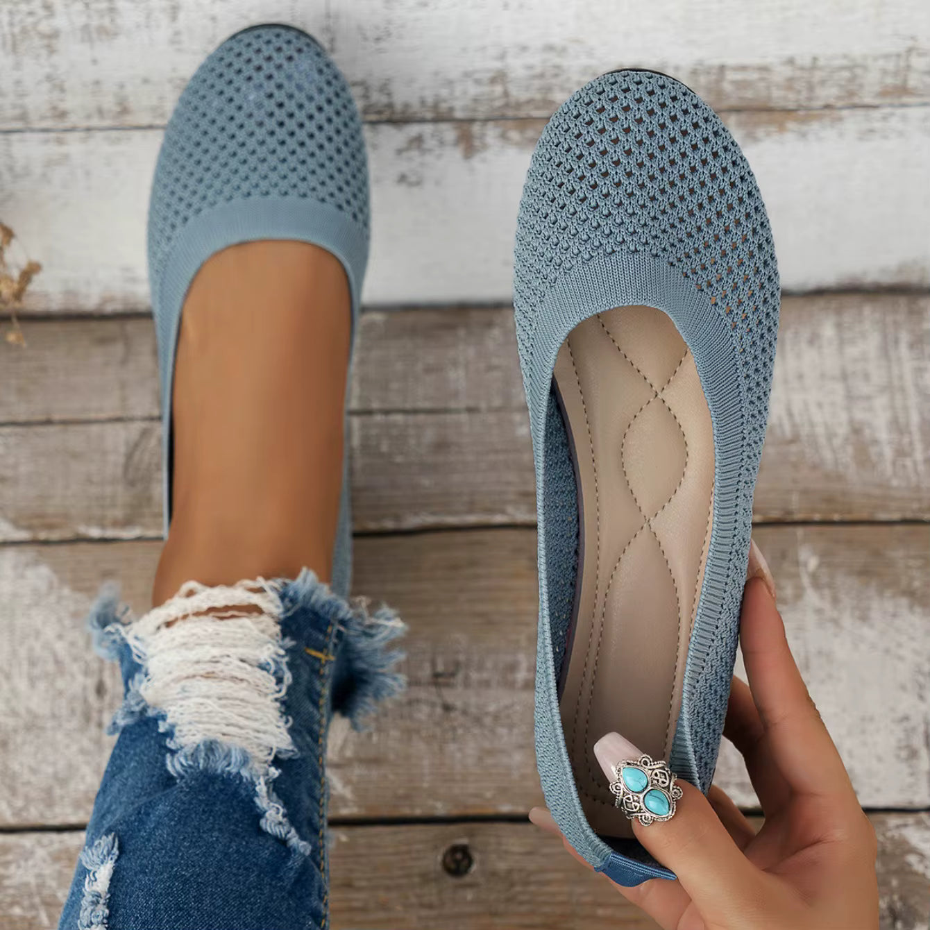 Blue textured flats held by a hand on a wooden floor