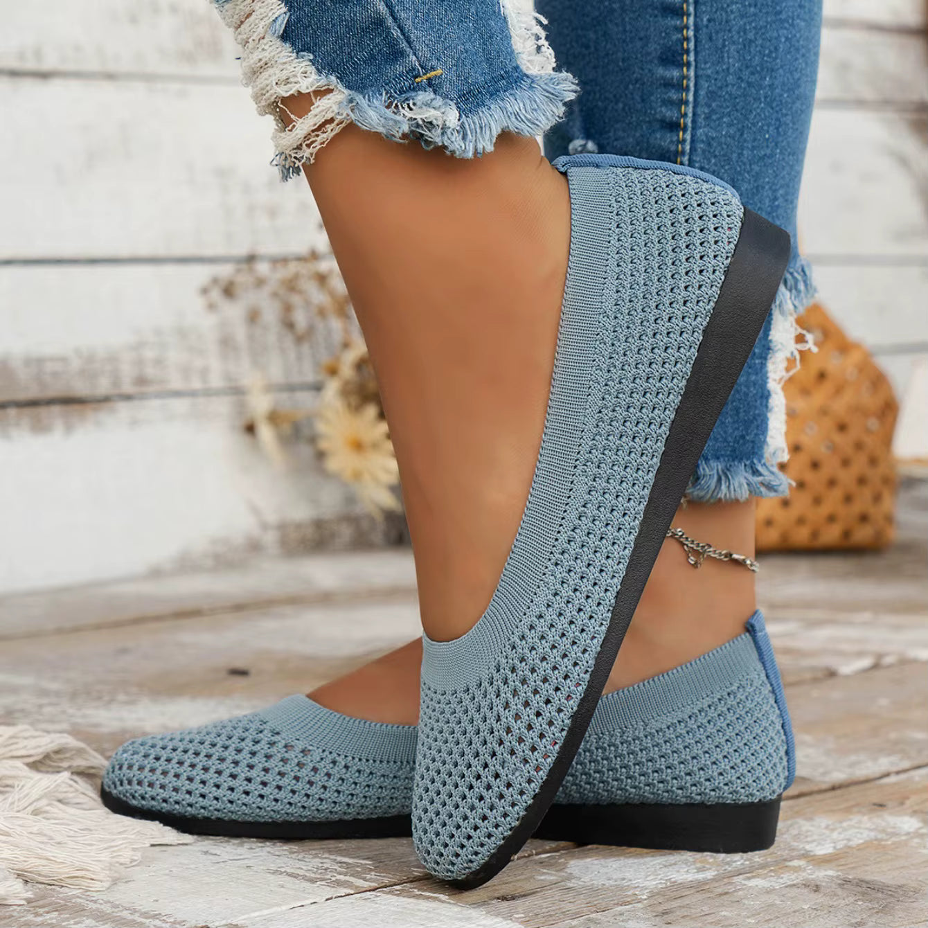 Blue knit shoes worn with ripped jeans on a wooden floor.