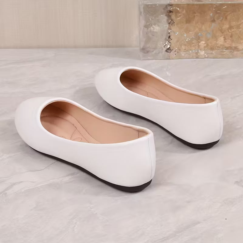 Pair of white flat shoes on a light gray surface with a neutral background