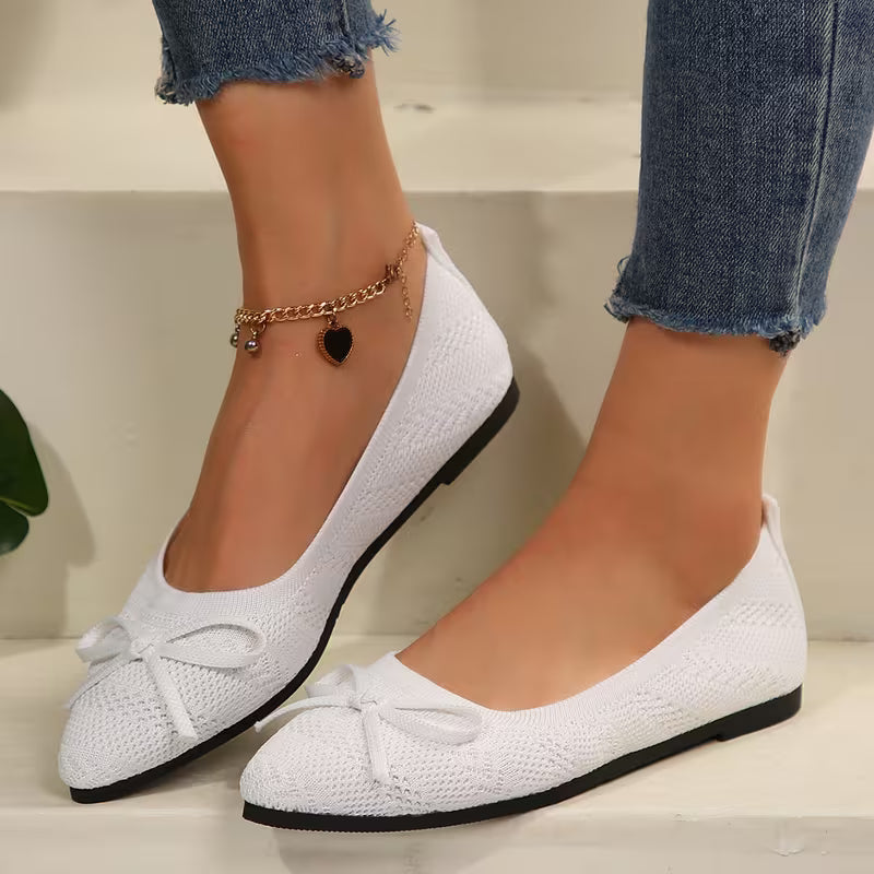 White flats with bows worn by a person, on a neutral background