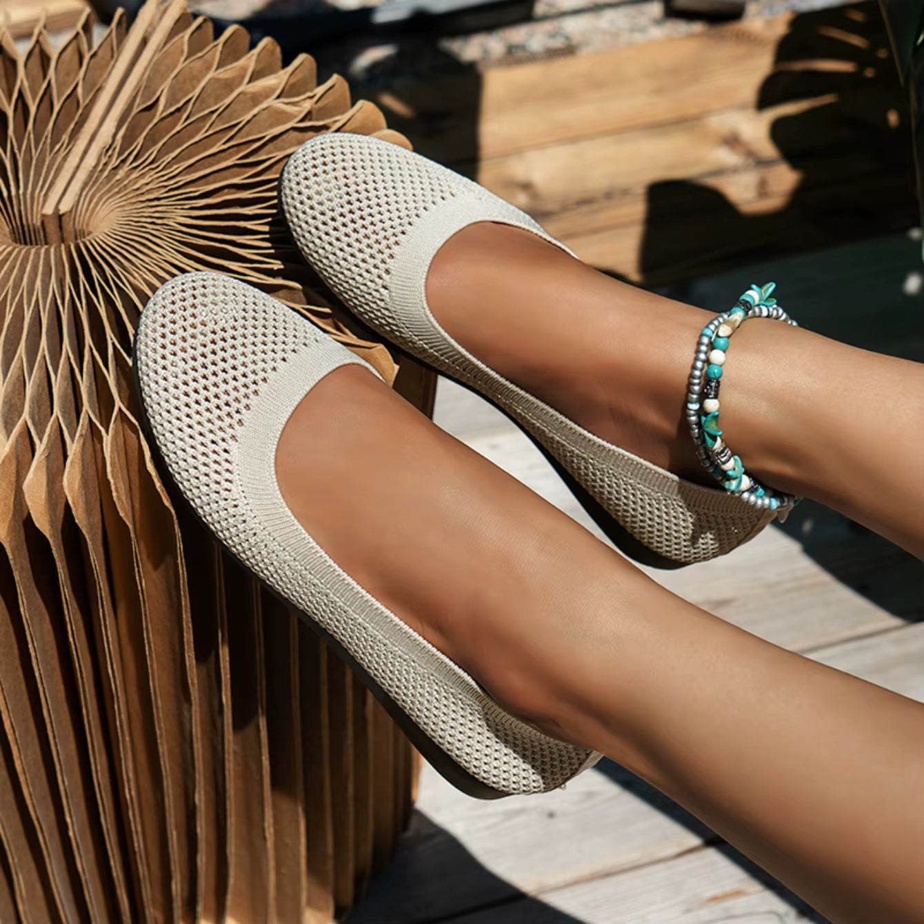 Beige woven shoes worn by a person sitting on a wooden bench.