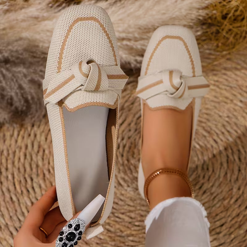Beige loafers with a knot detail worn by a person on a textured surface